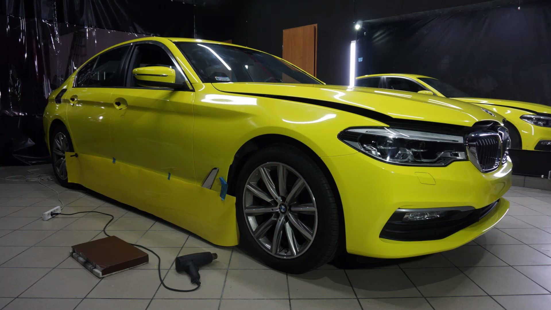BMW Serie 5 durante un vinilado en amarillo en el box del taller, con la pistola de calor en el suelo