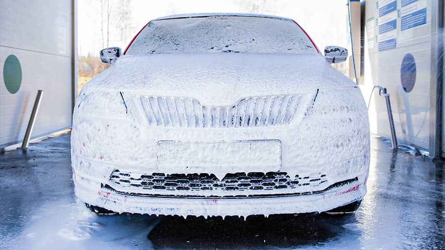 Carrocería de un coche cubierta de espuma durante el prelavado previo a la preparación de la pintura