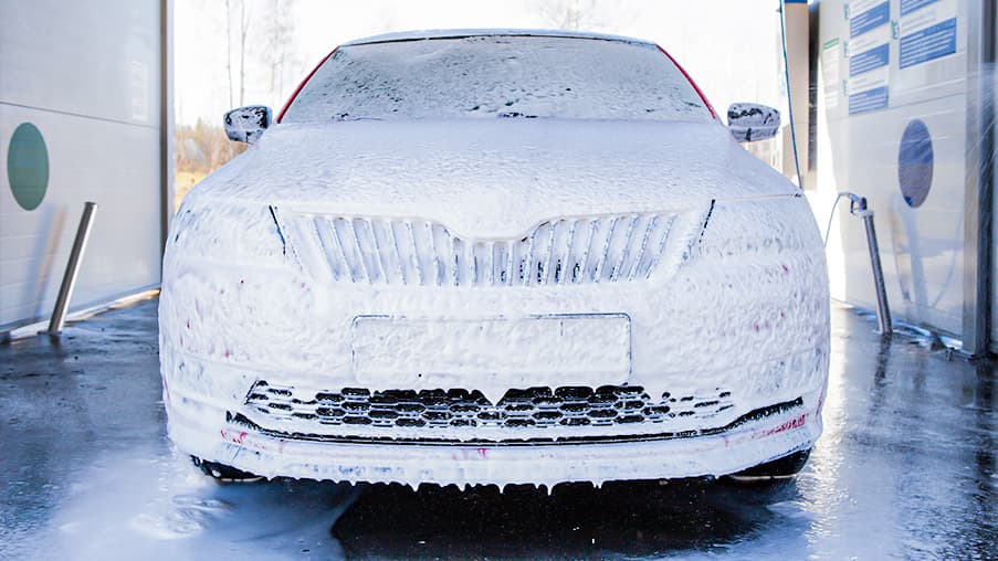 Carrocería de un coche cubierta de espuma durante el prelavado previo a la preparación de la pintura